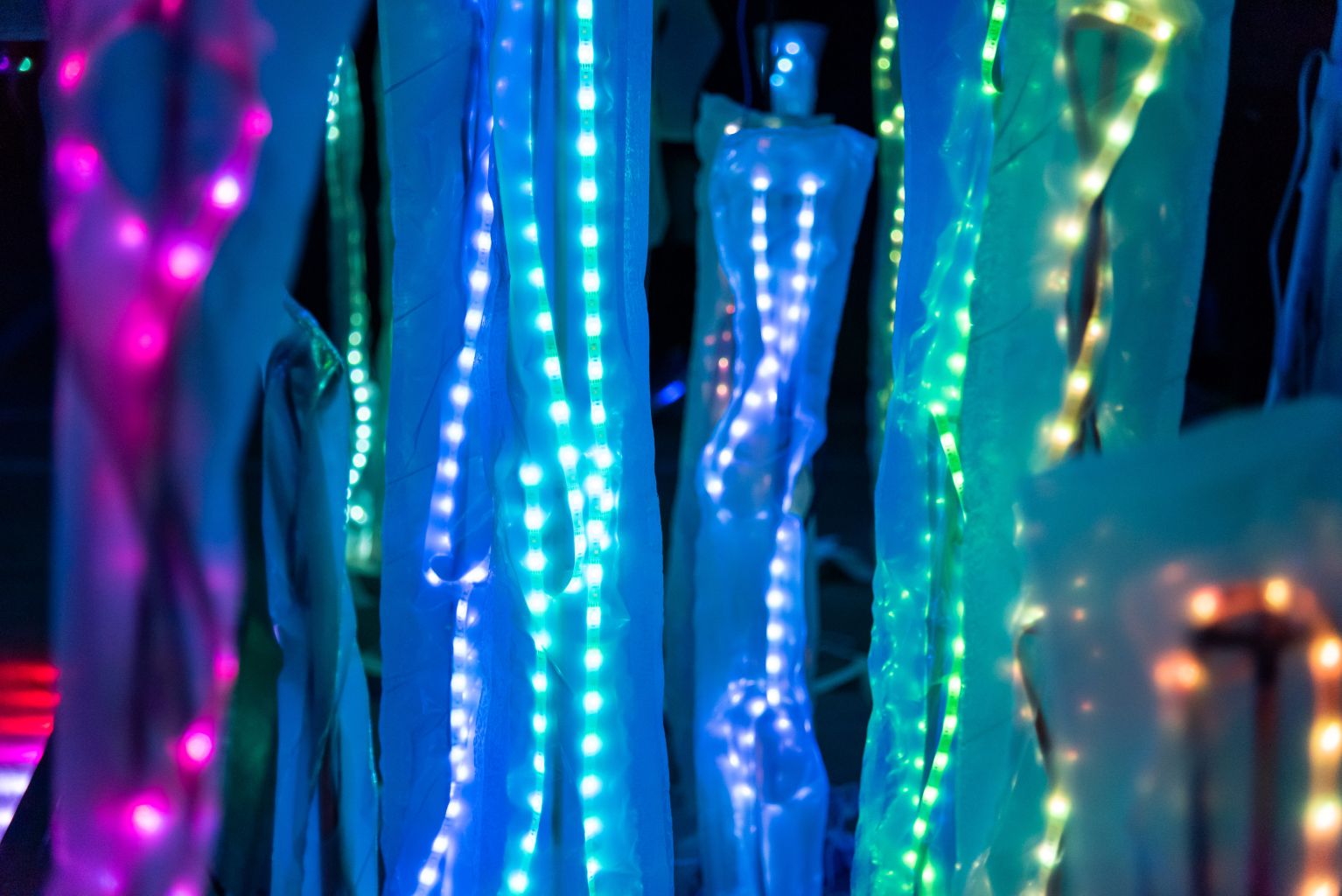 Art installation of sheer fabric tubes with LED lights inside illluminated at night